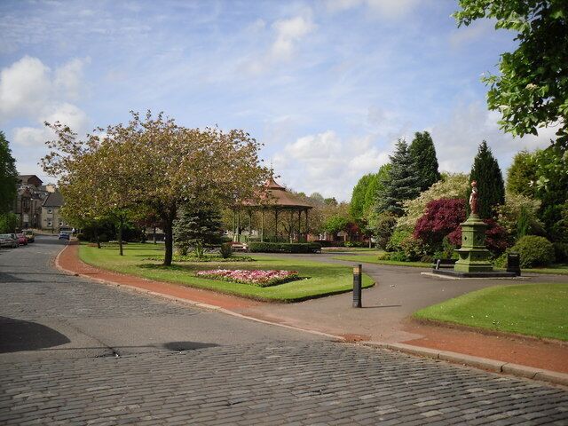 Uma rua de paralelepípedos, um parque com um coreto e uma estátua.