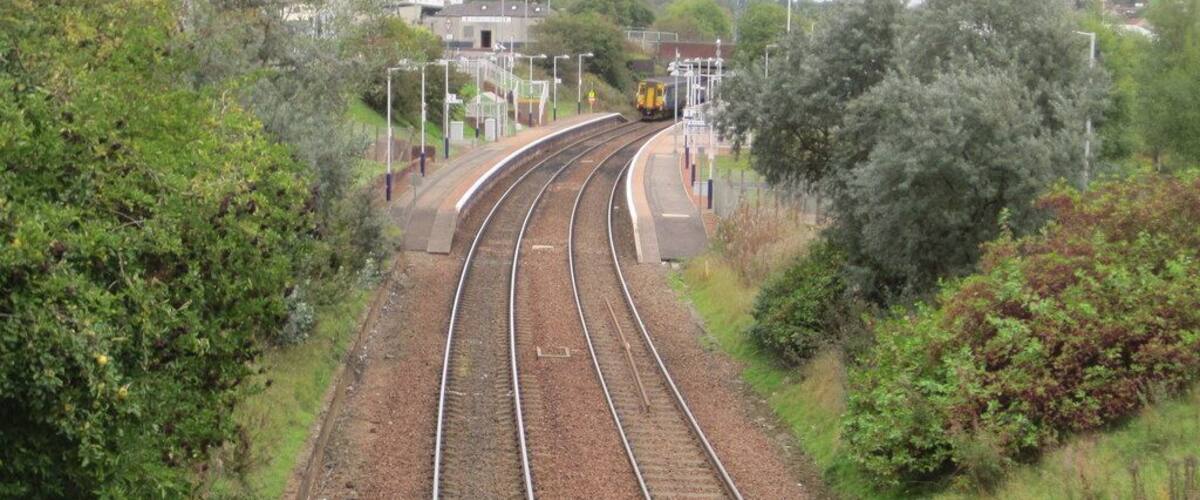 Railway tracks curving through a green landscape with trees and a building in the background.