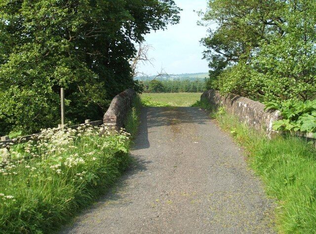 A narrow rural road flanked by stone walls and lush greenery.