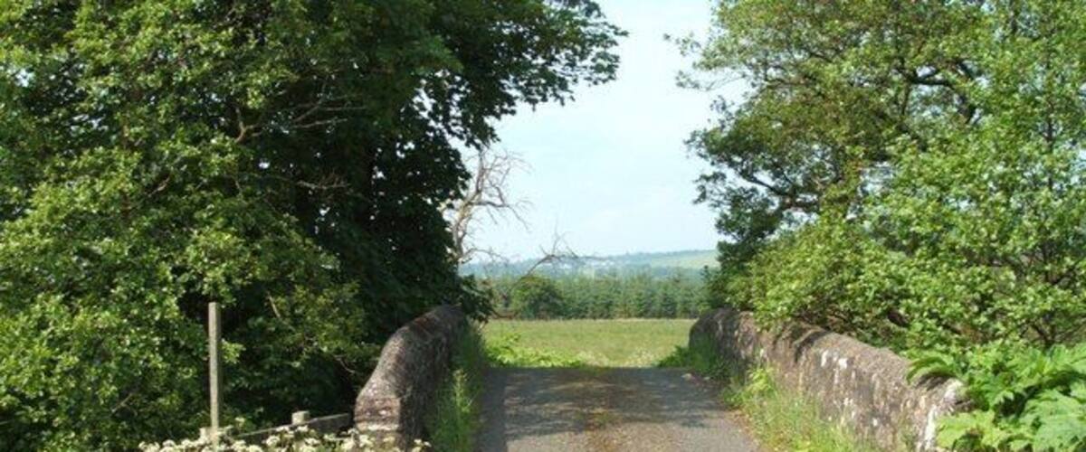 A narrow rural road flanked by stone walls and lush greenery.
