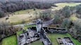 Vue aérienne d’un site historique comprenant des ruines, une tour de guet et une route sinueuse traversant un paysage rural.