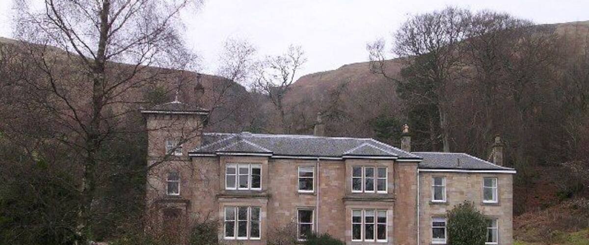 A large stone house with a well-maintained lawn and a hill in the background.
