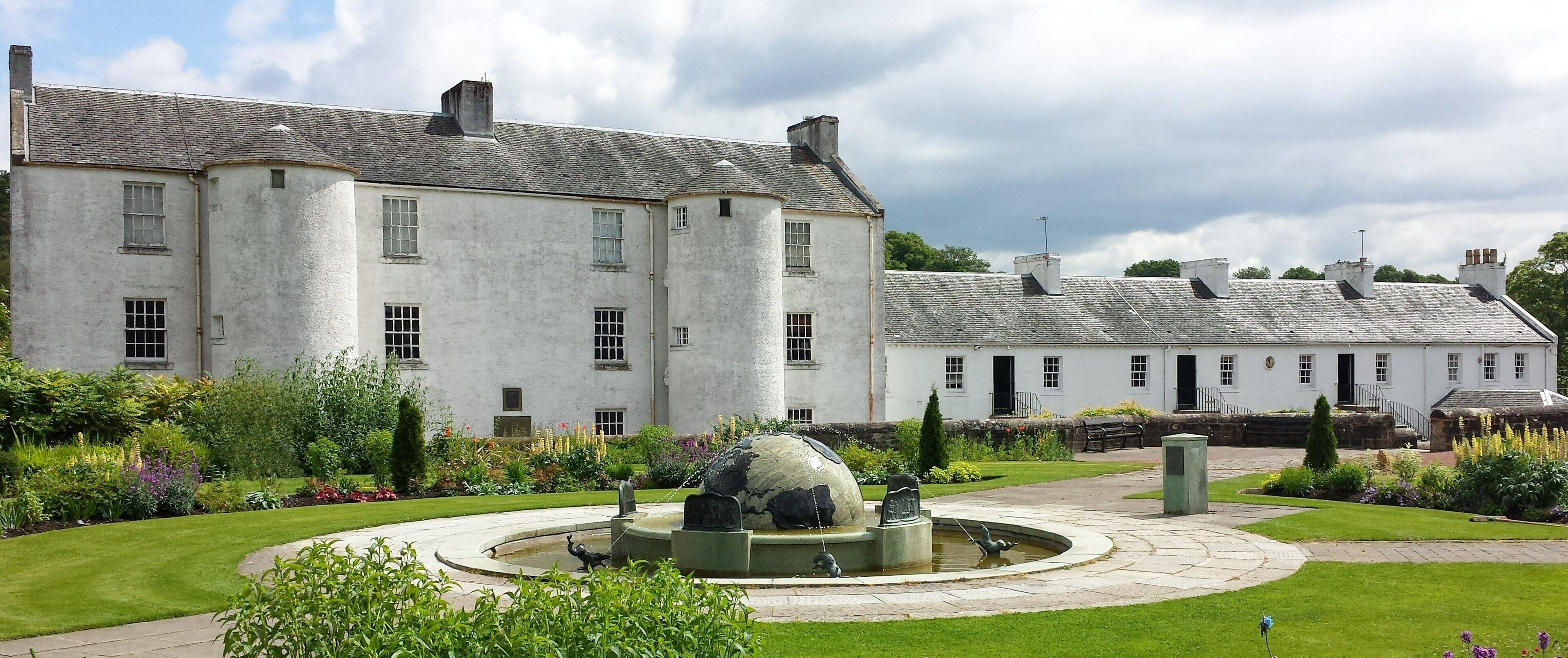 A large white building with a garden featuring a fountain and sculptures.