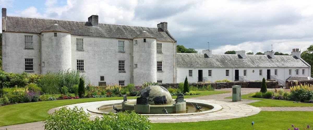 A large white building with a garden featuring a fountain and sculptures.