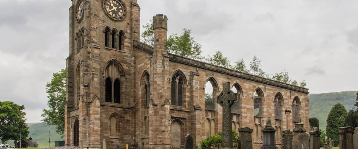 A historic stone church with a clock tower and a cemetery in the foreground.