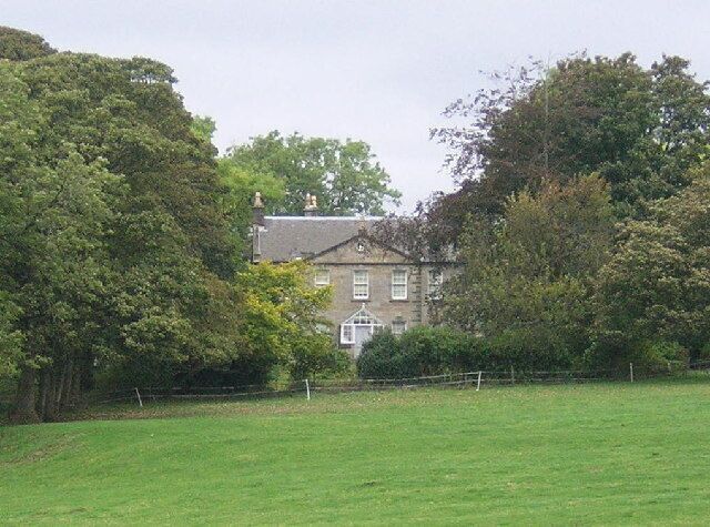 A large house surrounded by lush green trees and a grassy field.