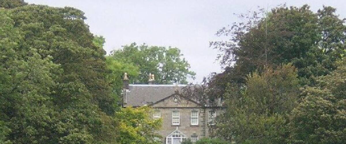 A large house surrounded by lush green trees and a grassy field.