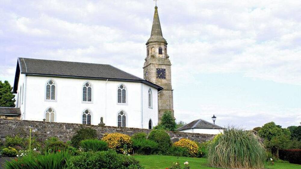 A white church with a clock tower, surrounded by a well-maintained garden with various plants and flowers.