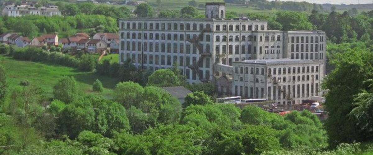 A large, multi-story building with a classical architectural style, surrounded by lush green fields and scattered houses.