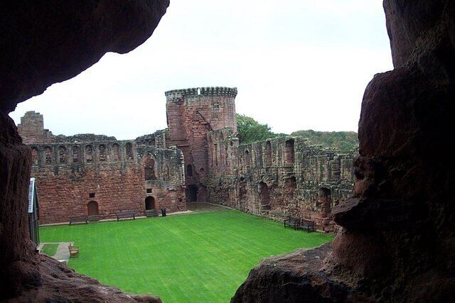 A historic castle with a central tower, a green lawn, and stone walls.