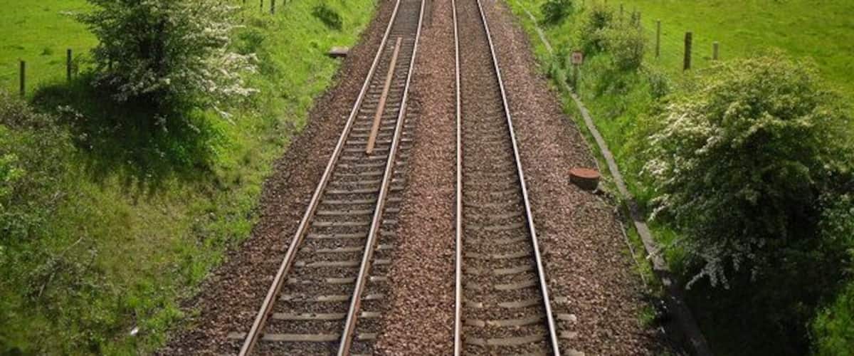 Railway tracks curving through a green landscape with fields and trees.