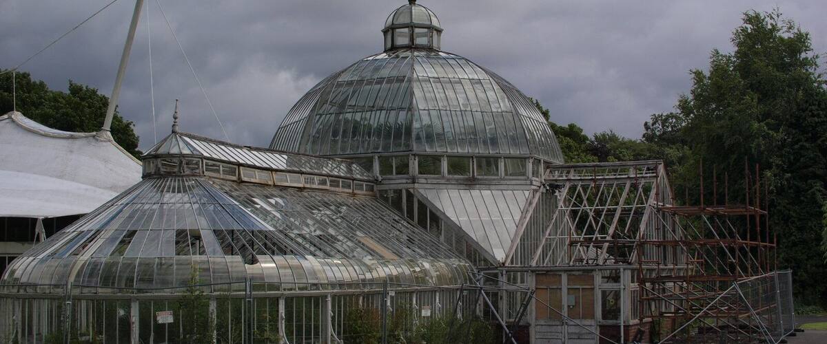 A large glass greenhouse with a dome roof, surrounded by scaffolding and a white tent.