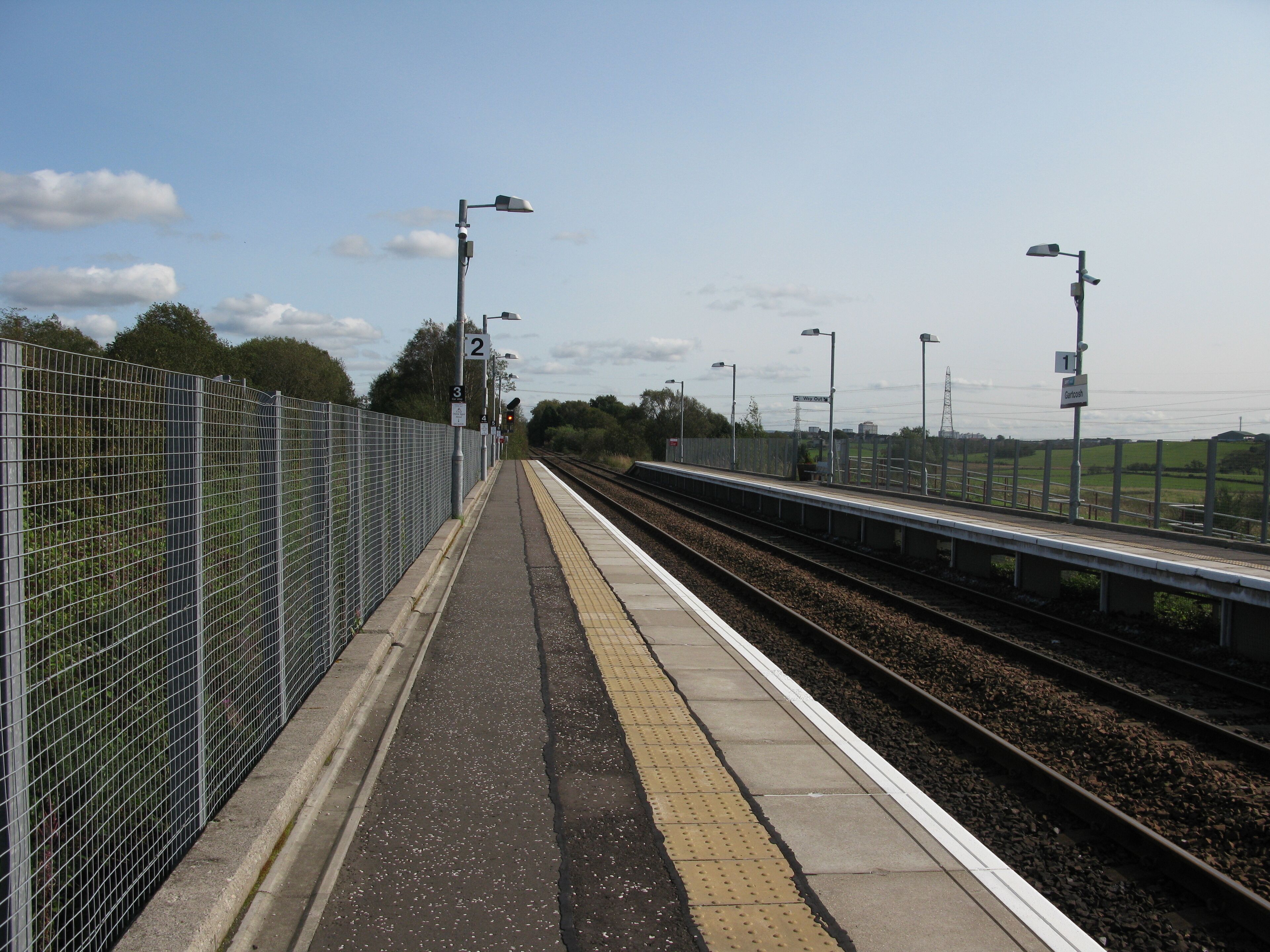 A railway platform with a fence, tracks, and street lamps.