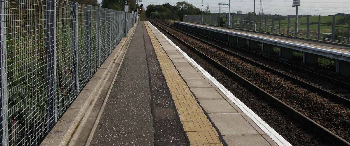 A railway platform with a fence, tracks, and street lamps.