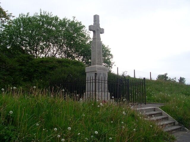 A stone cross monument surrounded by grass and dandelions.