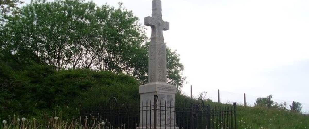 A stone cross monument surrounded by grass and dandelions.