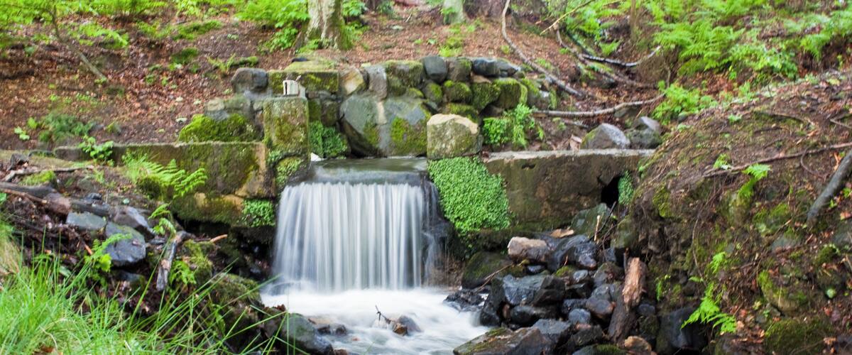 A small waterfall surrounded by rocks and greenery.
