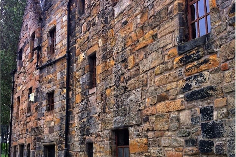A stone building with multiple windows and doors, surrounded by trees.