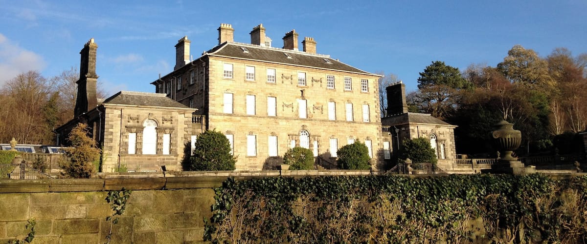 A large stone building with multiple chimneys and windows, surrounded by trees and a stone wall.
