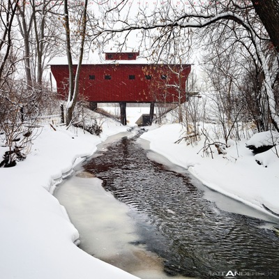 A short distance out of the small city of Milton, WI is a neat old wood covered bridge. It provides a little used road over a small meandering stream. On this Winter day we received over a foot of snow. The white flakes and the red bridge created one of my favorite Americana photos. The tree lined snowy path provides a surreal and wintery feel.