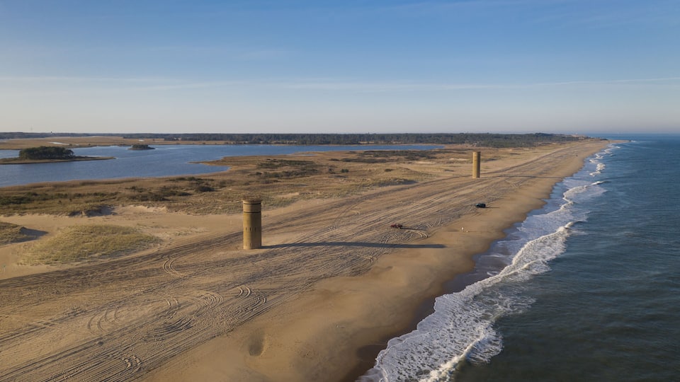A coastal landscape with a sandy beach, a lighthouse, and a calm sea.