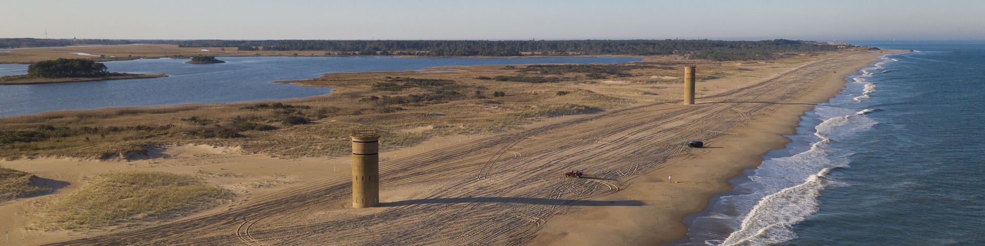 A coastal landscape with a sandy beach, a lighthouse, and a calm sea.