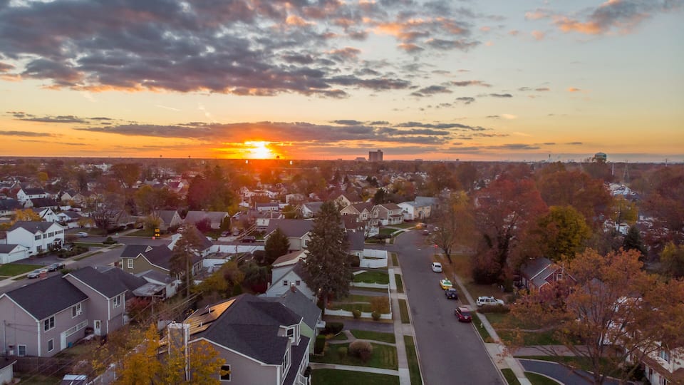 A suburban neighborhood at sunset with houses, trees, and a road.
