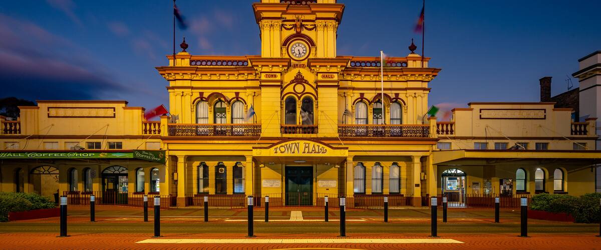 A historic town hall with a clock tower, surrounded by cobblestone streets and flagpoles.