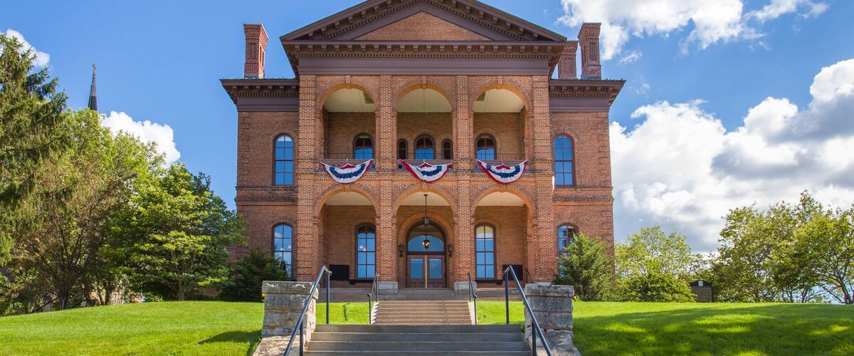 A large brick building with a central dome and arched windows, surrounded by green grass and trees.