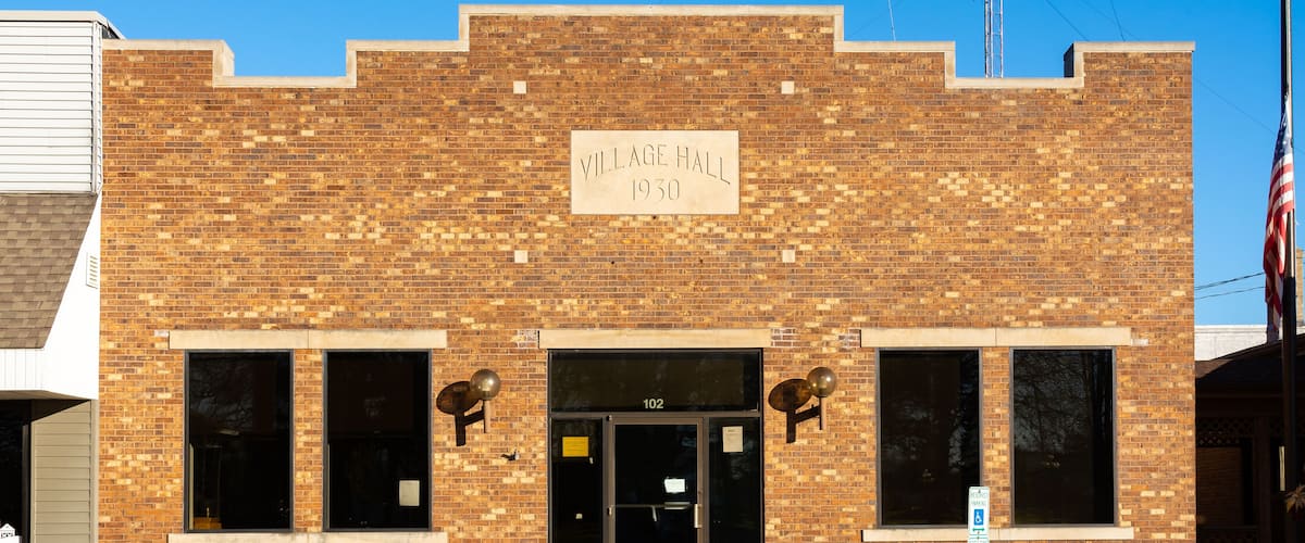 A brick building with a sign reading "Village Hall 1930" and the number "102" above the entrance.