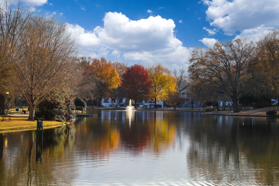 a water fountain in the middle of a still lake surrounded by red and yellow autumn colored trees in the park with fallen autumn leaves on the ground at Freedom Park in Charlotte North Carolina USA