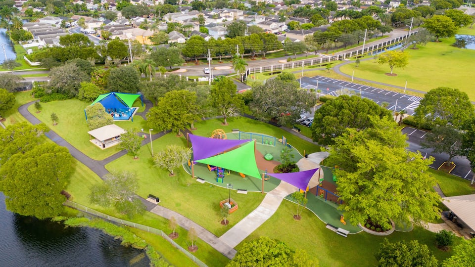 An aerial view of a park with playgrounds, a sports field, and a parking lot.