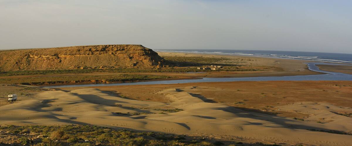 A desert landscape with sand dunes, a river, and a cliff.