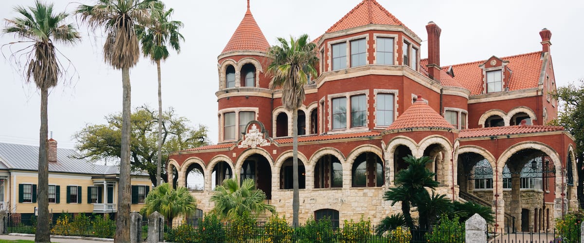 A large, historic mansion with a red-tiled roof, multiple arched windows, and a prominent tower.
