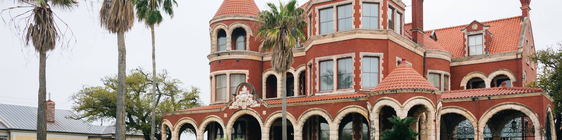A large, historic mansion with a red-tiled roof, multiple arched windows, and a prominent tower.