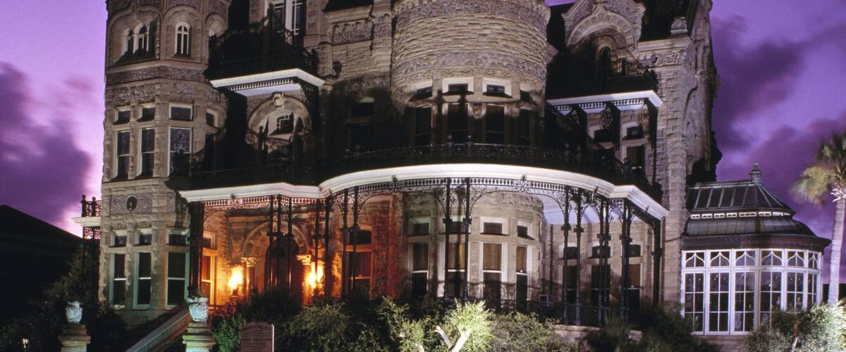 A large, ornate building with multiple towers and arched windows, illuminated at night.