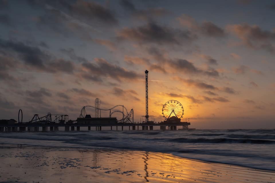 A pier with amusement rides and a Ferris wheel at sunset.
