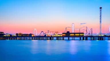 A pier with amusement rides and a Ferris wheel at dusk.