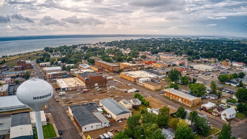An aerial view of a town with a water tower labeled 'MOBRIDGE', a river in the background, and various buildings and roads.