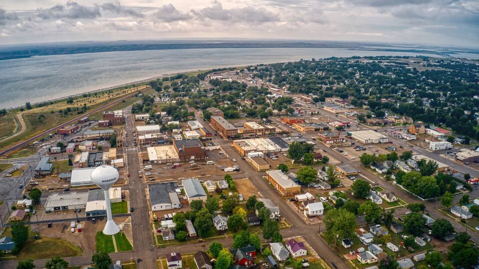 An aerial view of a town with a large water tower, a river, and a distant shoreline.