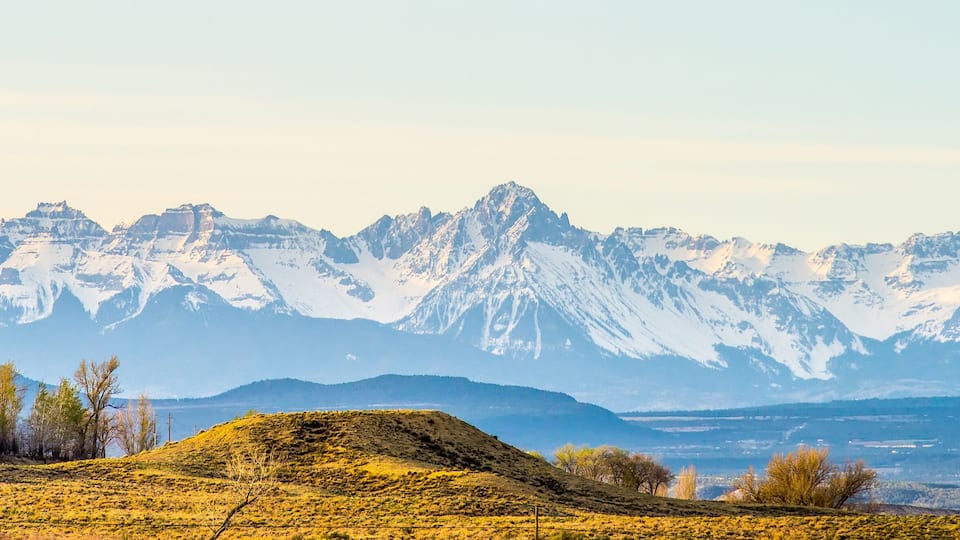 A mountain range with snow-capped peaks and a valley with sparse vegetation.