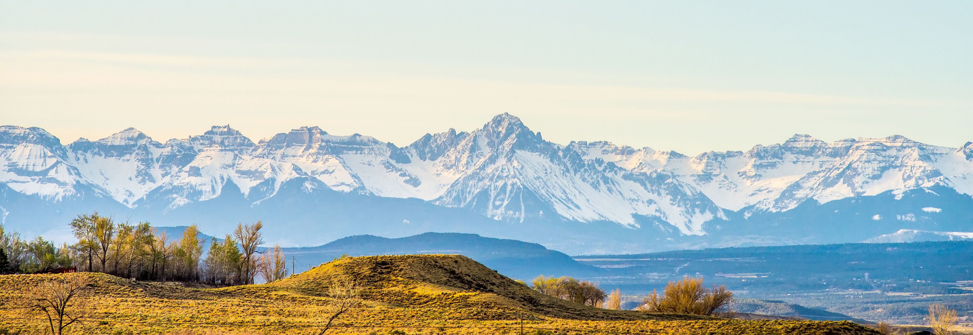 A mountain range with snow-capped peaks and a valley with sparse vegetation.