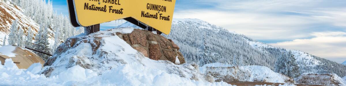 A sign at Monarch Pass indicating the Continental Divide between the Atlantic and Pacific Oceans, with San Isabel and Gunnison National Forests nearby.