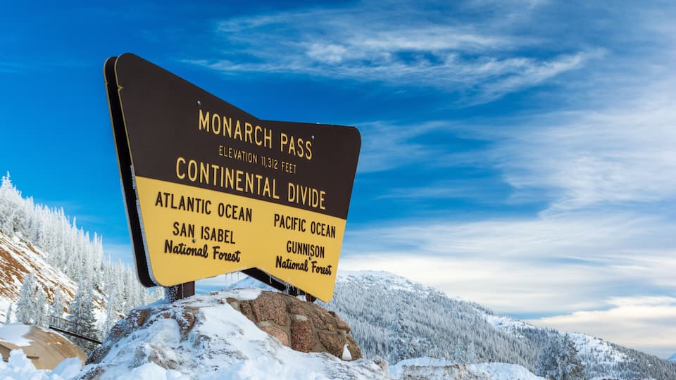 A sign at Monarch Pass indicating the Continental Divide between the Atlantic and Pacific Oceans, with San Isabel and Gunnison National Forests nearby.