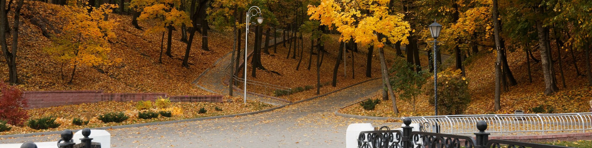 Un sendero pavimentado con barandillas negras decorativas, rodeado de árboles con follaje otoñal.
