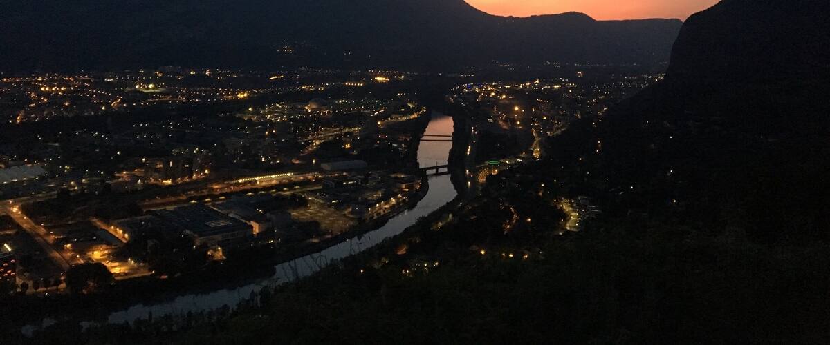 A cityscape at dusk with a river running through it, surrounded by mountains.