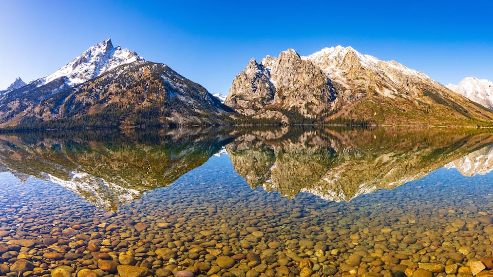 A mountain range reflected in a clear lake with visible rocky lakebed.