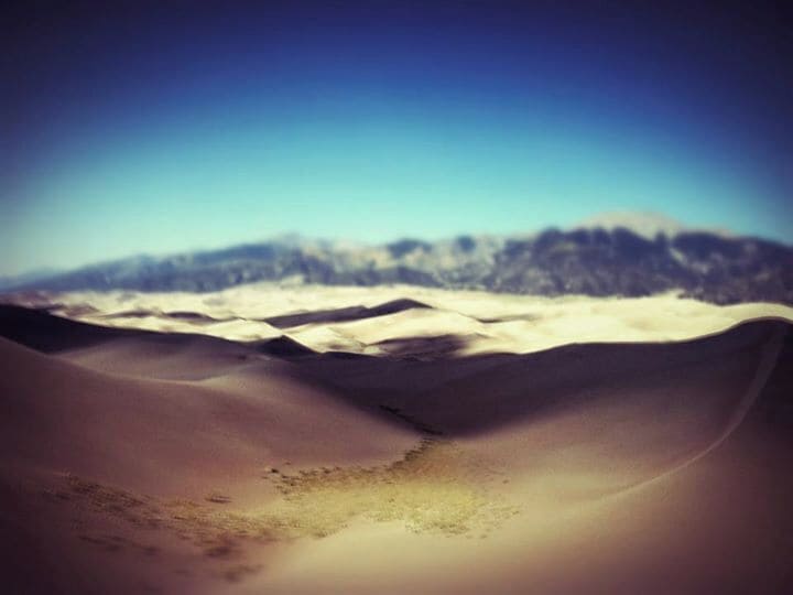 A desert landscape with sand dunes and a mountain range in the background.