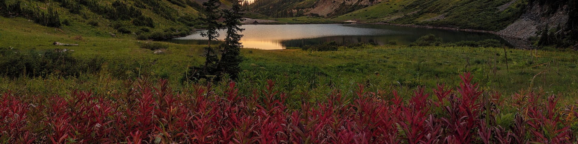 A lake surrounded by mountains, with red foliage in the foreground.