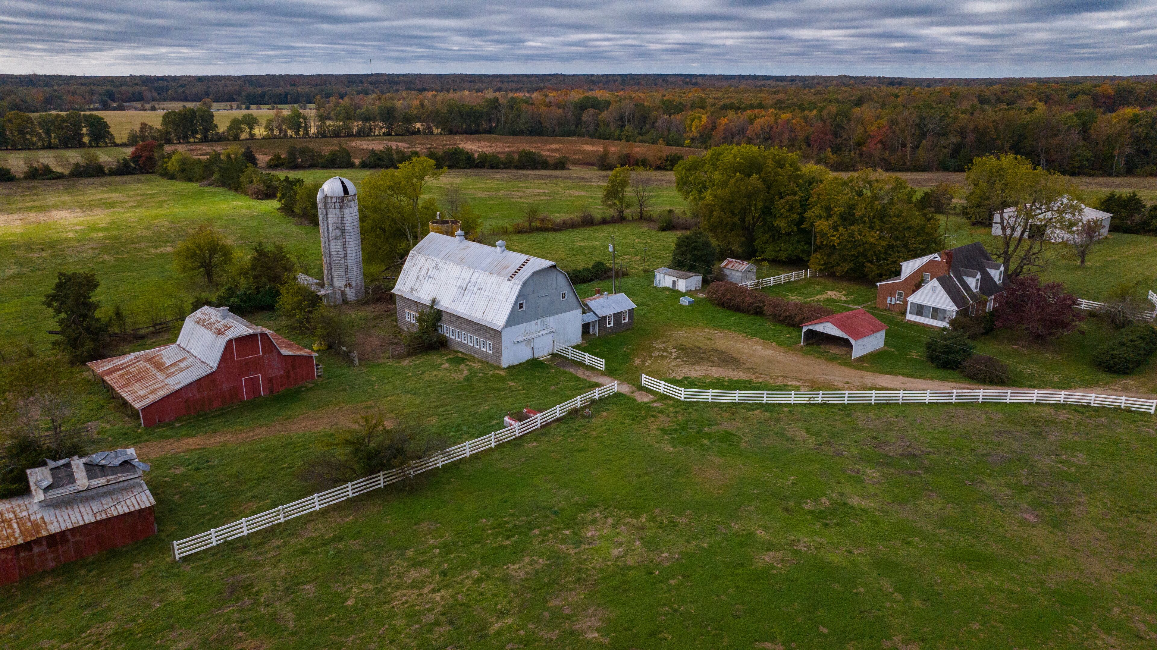 A rural farm with barns, a silo, and a white fence.